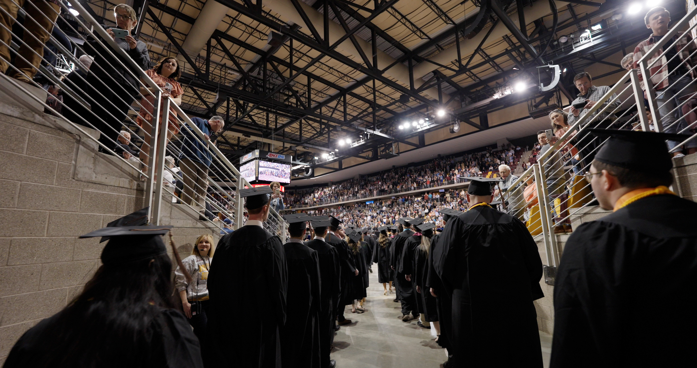 Graduating students in cap and gown in two lines waiting to enter the arena.
