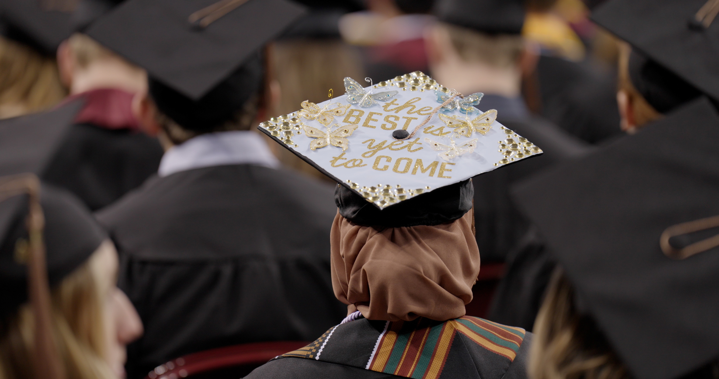 Group of graduates with a decorated cap reading, "The best is yet to come." in focus.